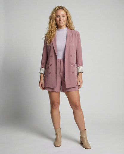 Woman wearing a pink blazer and shorts set with beige boots on a plain background
