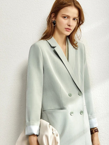 Close-up of woman in mint green pantsuit and white blouse, holding a white handbag