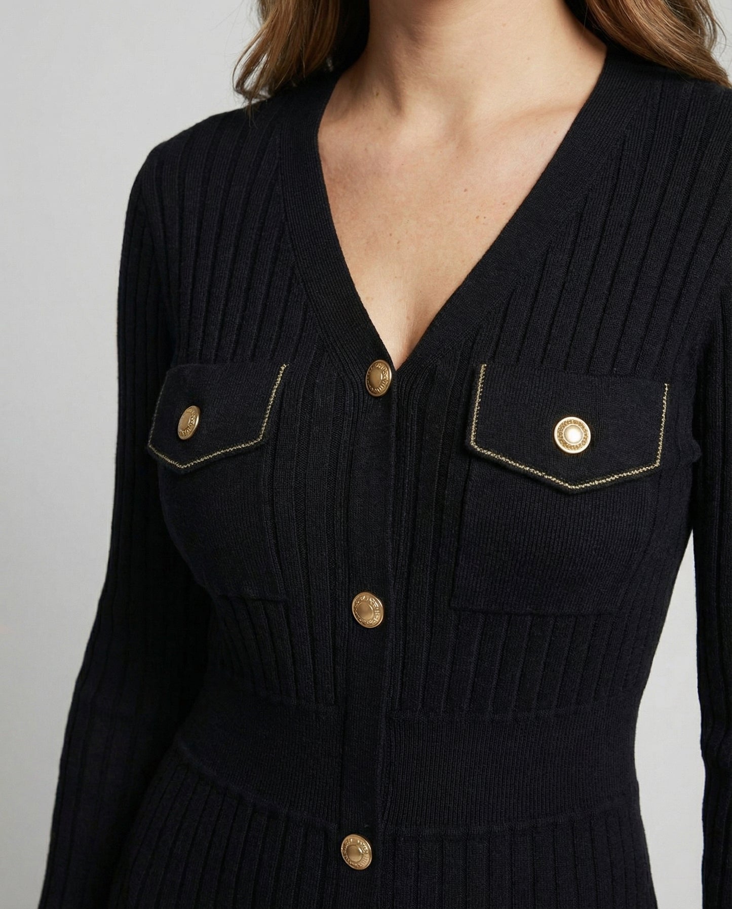 Black ribbed sweater with gold buttons on a gray background