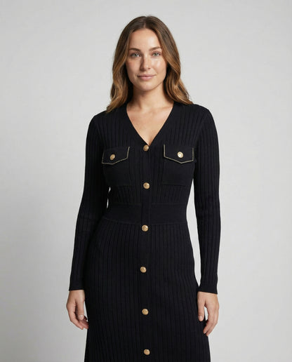 Woman wearing a black ribbed dress with gold buttons on a gray background