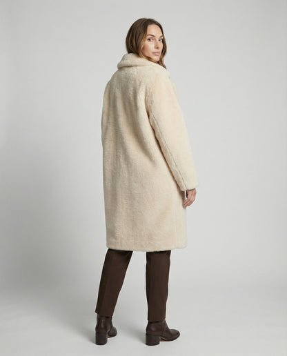 Woman wearing a cream-colored coat on a plain background