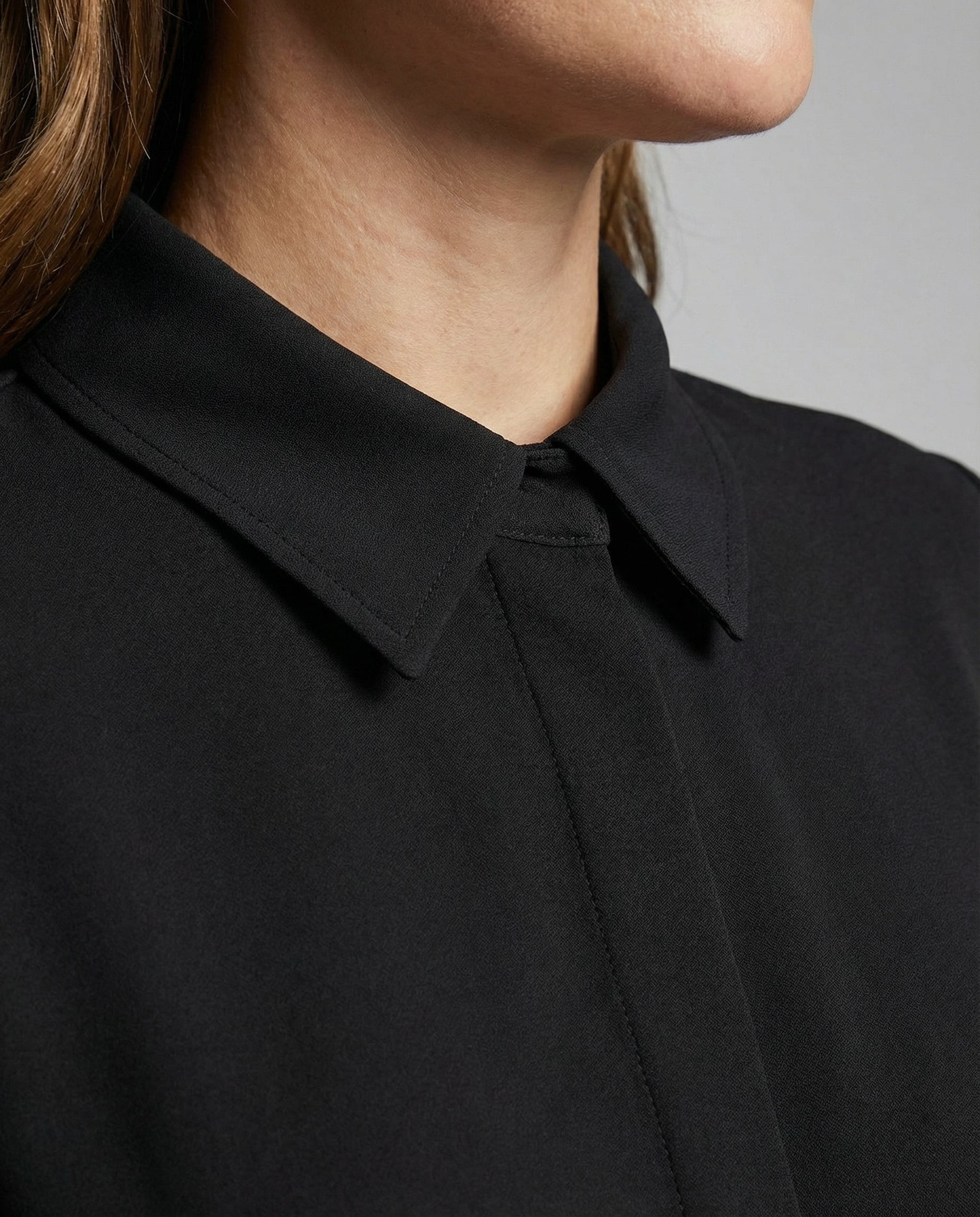 Close-up of a person wearing a black shirt with a collar against a neutral background