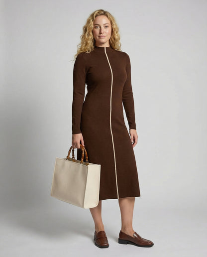 Woman wearing a brown dress holding a beige handbag against a plain background