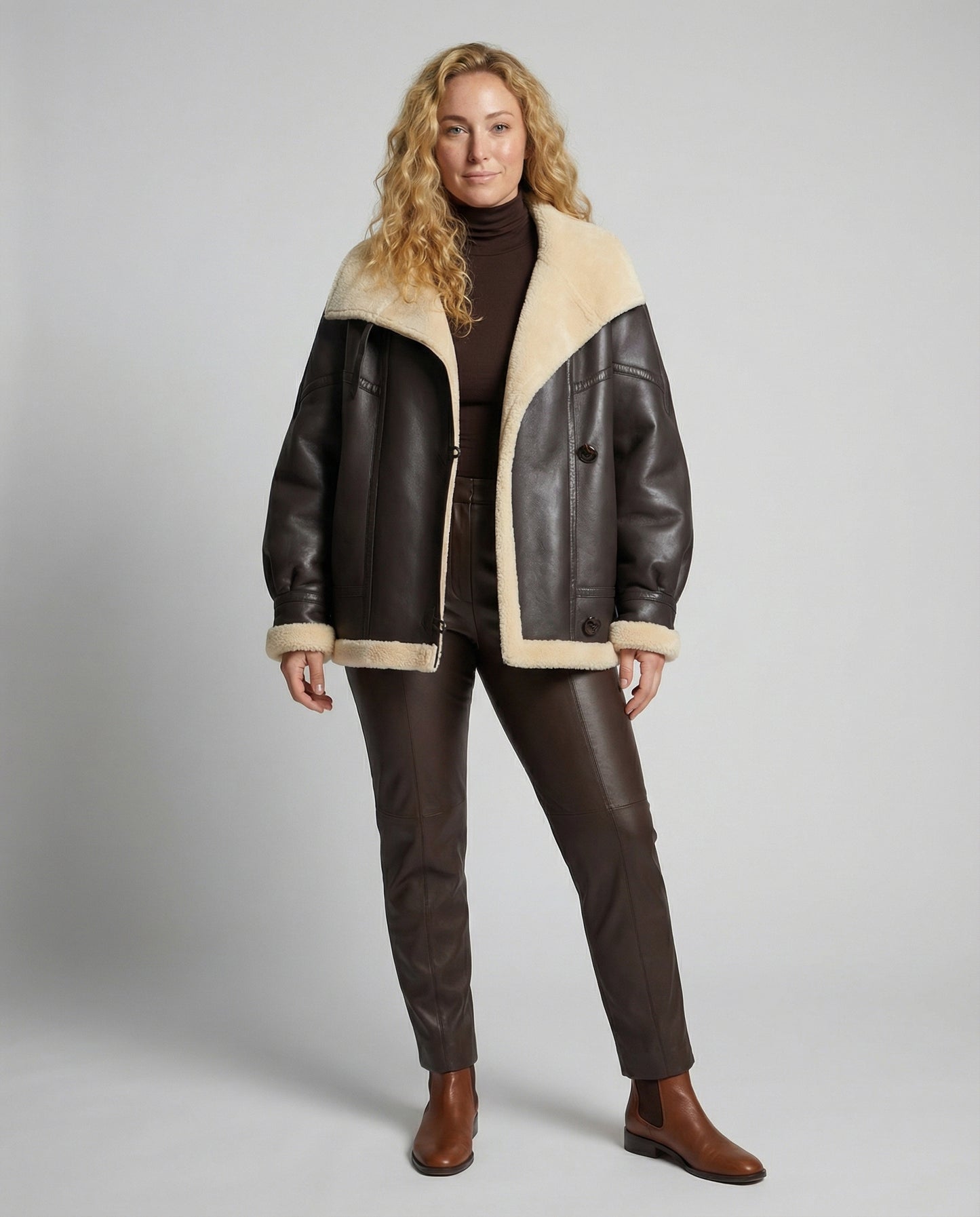 Woman wearing a brown leather jacket with beige fur lining on a gray background