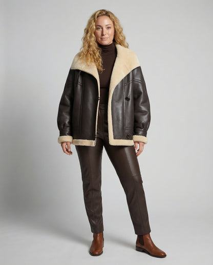 Woman wearing a brown leather jacket with beige fur lining on a gray background